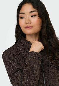 Pruun tekstuuriga jakk krae ja ees oleva tõmblukuga. Omab kootud mustrit ning trukiga detaili varrukamansetil.