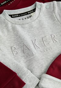 Szary bawełniany sweatshirt z haftowanym logo "BAKER"; posiada burgundowe akcenty na rękawach i napy na ramieniu. Miękka tekstura.