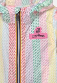 K-Way vindjacka med en lättviktig, flerfärgad design med ett upprepande logomönster, dragkedjestängning och en framträdande märkesapplikation.