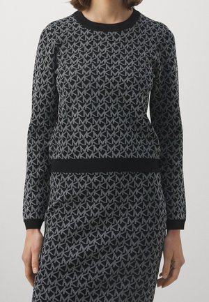 Femme portant un pull moulant manches longues noir et gris avec un motif géométrique répétitif et une jupe assortie.