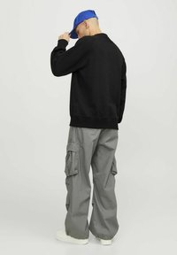 Zwarte sweatshirt met een ronde hals, gecombineerd met losse grijze cargo broek met zijvakjes en elastische boorden. Blauwe pet achterstevoren gedragen.