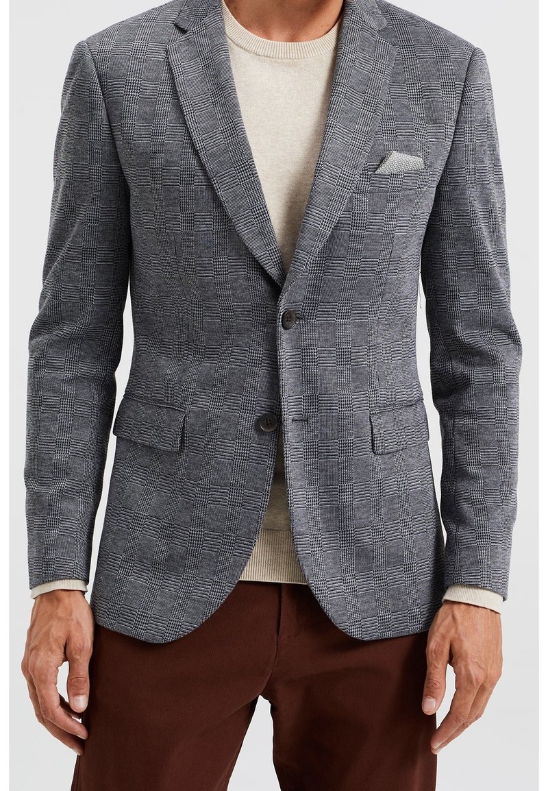 Grå rutig blazer med skräddarsydd passform, notchade slag, tvåknappsstängning och sidfickor. Bärs över en ljusbeige tröja.