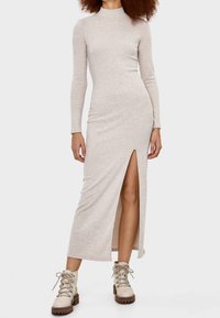 Lång, figurnära, beigeblå ribbad klänning med hög hals och sidoslits, i kombination med krämfärgade snörstövlar med en tjock klack.