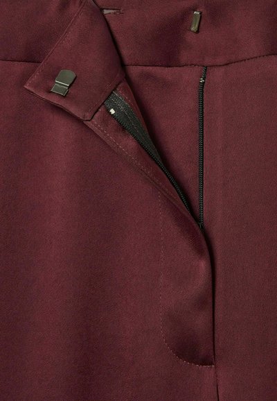 Indumento color bordeaux con cerniera nascosta e chiusura metallica. Tessuto liscio con una finitura leggermente strutturata e cuciture precise.