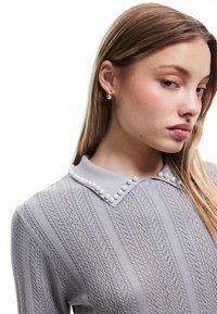 Szary, dziany sweter z teksturowanym wzorem oraz kołnierzem ozdobionym perłowymi detalami. Materiał jest lekki, a krój dopasowany.