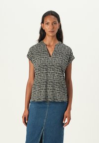 Short-sleeve blouse in black and white with a textured grid pattern, featuring a V-neckline and a loose fit. Paired with a denim skirt.