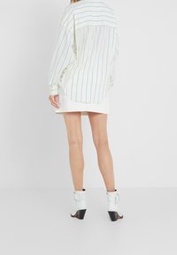 Camicia bianca a righe con maniche lunghe, caratterizzata da righe verdi e orlo curvo, abbinata a una mini gonna bianca e stivali bianchi con tacco.