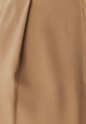 Hellbrauner strukturierter Stoff mit diagonalem Gewebe, der einen dezenten Glanz und eine glatte Oberfläche aufweist. Entlang einer Seite ist eine Kantennaht sichtbar.