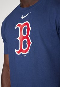 T-shirt in cotone blu navy con un grande logo rosso "B" con contorno bianco, logo Nike sopra in bianco. Maniche corte, design con scollo rotondo.
