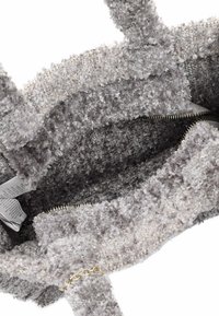 Borsa tote grigia in peluche con una texture morbida e soffice, tasca con zip e manici corti. L'interno mostra una fodera in tessuto e un'etichetta.