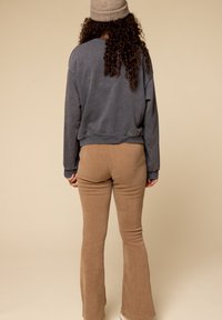 Grijze katoenen sweatshirt met verlaagde schouders en ribgebreide manchetten, gecombineerd met lichtbruine ribgebreide flared broek. Het model draagt een beige gebreide muts.