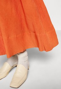 Oranžová sukně s texturou a detaily na spodním lemu, v kombinaci s krémovými koženými loafers a bílými žebrovanými ponožkami.