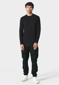 Svart långärmad tröja med rund halsringning, parat med svarta cargobyxor med sidfickor och elastiska muddar; vita sneakers.