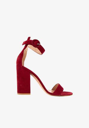 Sandale à talon haut en daim rouge, talon bloc, bout ouvert, bride à la cheville et boucle ronde sur fond blanc.