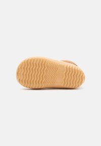 Suela de zapato de goma en tono marrón con un patrón texturizado en zigzag y un detalle de logo rectangular. Los bordes circulares aportan estabilidad y agarre.