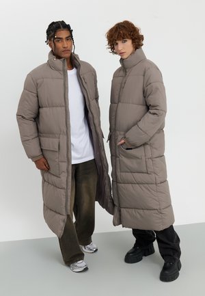 Dolgi pufasti plašči v taupe barvi z diagonalno prešitimi občutki. Imajo visoke ovratnike, stranske žepe in sproščen kroj. Nosi se preko vsakodnevnih oblačil.