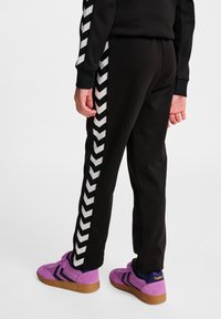 Zwarte jogerpants met een wit chevronpatroon langs de zijkant, van zachte stof en met een elastische tailleband. Gemaakt in combinatie met paarse sneakers.