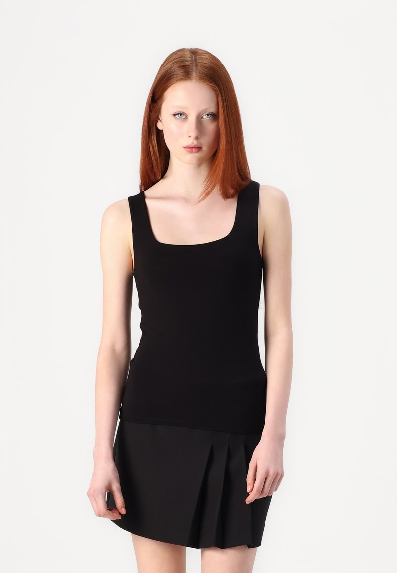 Zwarte mouwloze tanktop met een vierkante halslijn, gemaakt van gladde stof. Het model draagt het met een geplooide zwarte minirok.