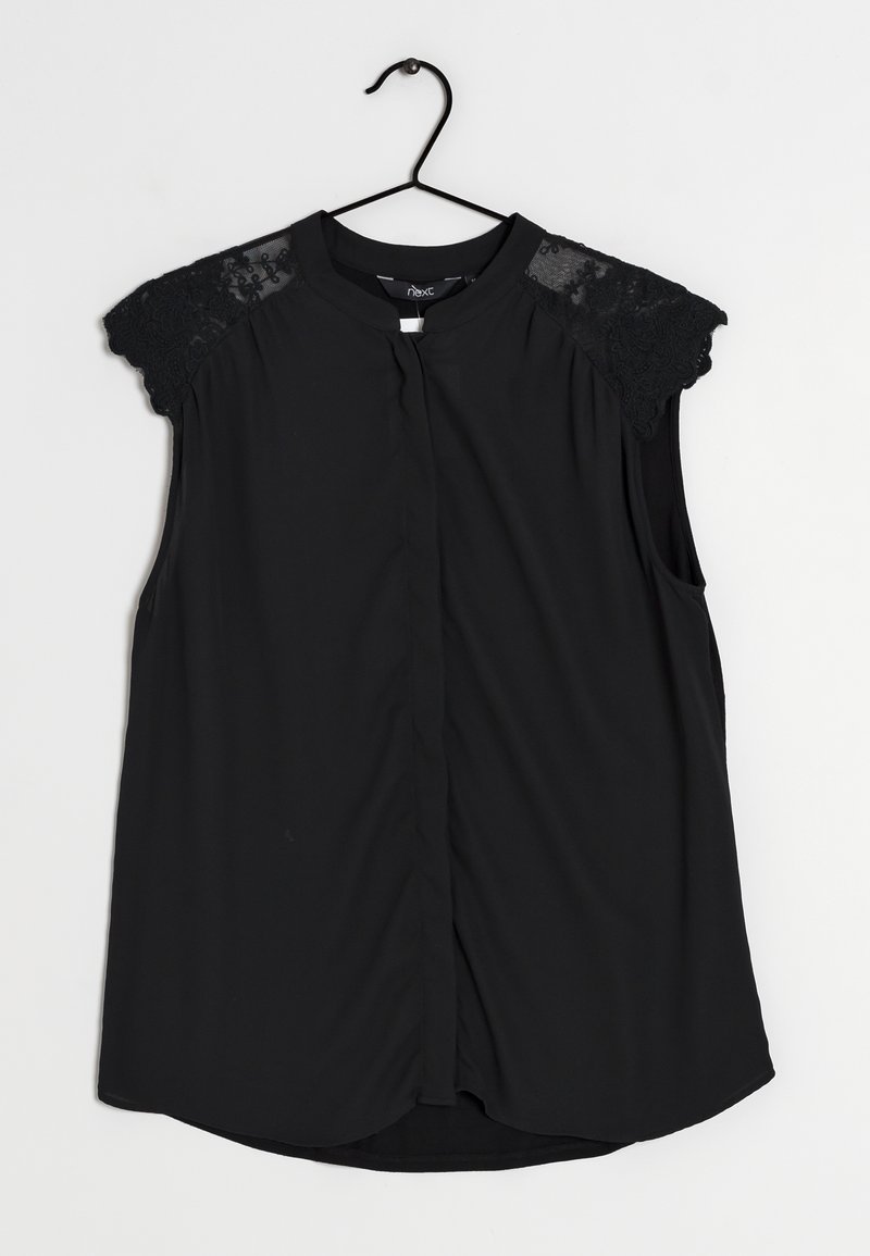 Blouse noire à manches courtes, avec des accents en dentelle transparente sur les épaules, fermeture avant par boutons et ourlet arrondi.