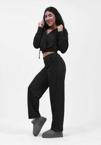 Sudadera cropped negra con cordones, combinada con pantalones jogger negros y pantuflas grises de felpa. Tejido suave con un corte relajado y bolsillos.