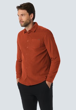 Rustkleurig corduroy shirt met een button-down kraag, een opgestikte zak en lange mouwen, gecombineerd met zwarte broek.