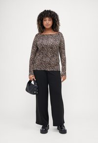 Leopard-print long-sleeve top with a wide neckline, paired with loose black trousers. Accessories include a small black handbag and chunky shoes.