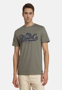Oliven grøn bomulds t-shirt med korte ærmer, rund halsudskæring og navy blå "Petrol & Co" grafisk print på forsiden.