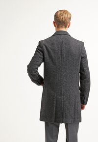 Tmavě šedý vlněný kabát s dlouhým střihem, s klopami a hladkou texturou. Disponuje přiléhavým střihem a jedním rozparkem na zadní straně.