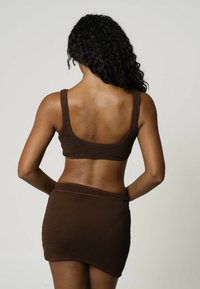 Ruskea ribattukangas kaksiosainen asuste, johon kuuluu istuva crop-top ja siihen sopiva mini-hame, korostaen saumatonta muotoilua ja teksturoitua materiaalia.