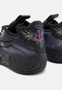 Baskets noires de sport avec une tige texturée, ornées d'un emblème coloré en forme d'aile et d'une semelle noire sculptée avec des motifs complexes.