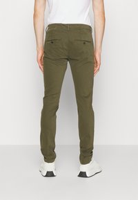 Olivgröna bomullsbyxor med slim fit, två bakfickor och en mjuk yta, matchade med vita sneakers.