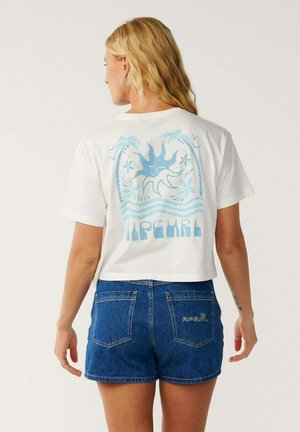 Vrouw met lang blond haar draagt een wit cropped t-shirt met een blauw zon- en palmboomontwerp en blauwe denim shorts met achterzakken.