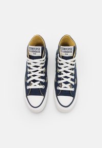 Baskets montantes en toile navy avec semelle en caoutchouc blanche, accents de broderie dorée et lacets blancs. Doublure jaune visible à l'intérieur.