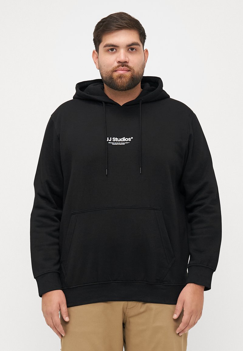 Zwarte hoodie van katoen, met een voorzak, trekkoordcapuchon en witte "JJ Studios" logo in het midden. Zachte textuur, casual fit.