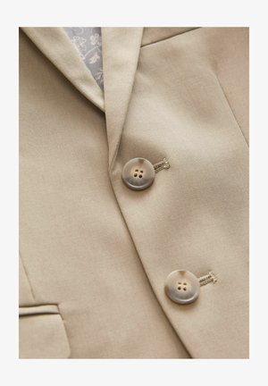Halványbarna blézer sima textúrával, tépőzáras gallérral, két barna gombbal, mindkettő négy lyukkal, világos színű varrással kiemelve.