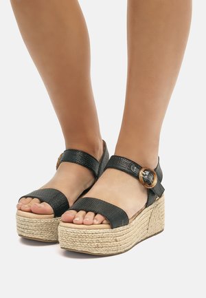 Schwarze Keil-Sandalen mit einem gewebten Jute-Plateau, ausgestattet mit strukturierten Riemen und einem Akzent in Goldfarbe an der Schnalle. Offenes Zehendesign.