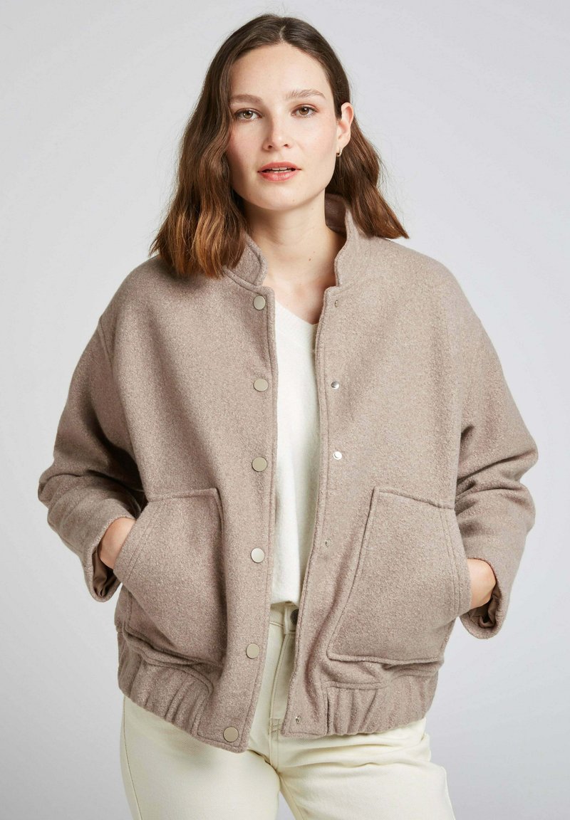 Veste en polaire beige avec un devant à boutons, un ourlet côtelé et des poches latérales. Caractérisée par un col haut et une coupe décontractée.
