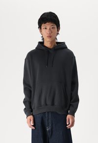 Sweat-shirt à capuche noir en tissu en mélange de coton. Il possède une poche kangourou, des poignets et une taille côtelés. Texture lisse et coupe décontractée.