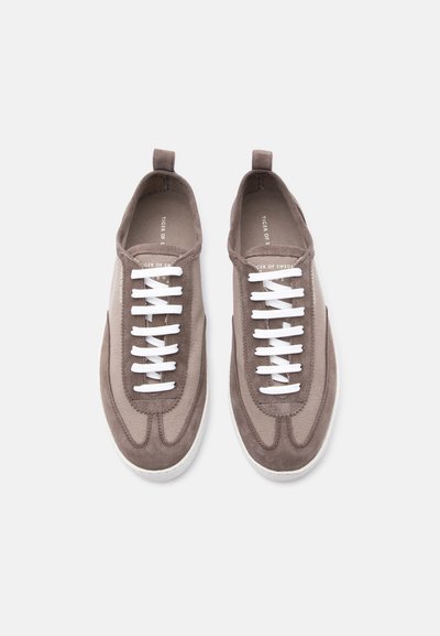 Ζευγάρι καφέ σουέντ και υφασμάτινα αθλητικά παπούτσια με λευκά κορδόνια, στρογγυλές μύτες και θηλιές στο πίσω μέρος, σε απλό λευκό φόντο.