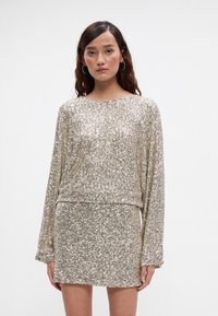 Obleka s sekvinskim vzorcem, dolgimi rokavi, okroglim izrezom in prilegajočim silhueto. Barva: kovinsko zlata, s sijočo, teksturirano površino.