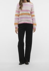 Gestreifte Sweatshirt in Pink, Orange und Creme mit einer flauschigen Textur; kombiniert mit schwarzen weiten Hosen und flachen schwarzen Schuhen.