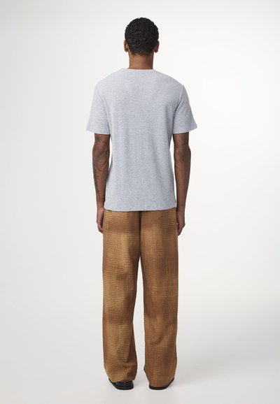 Grå kortærmet T-shirt parret med brune mønstrede brede benbukser. Stoffet har en subtil tekstur, der tilføjer dybde til sættet.