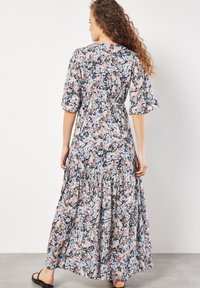 Blumiges Maxikleid mit kurzen, ausgestellten Ärmeln, einem taillierten Oberteil und einem geschichteten, rüschenbesetzten Rock in Blau-, Pink- und Cremetönen auf dunklem Hintergrund.