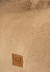 Texture in pelliccia sintetica beige con superficie liscia e morbida e un'etichetta quadrata in pelle con logo a stella in rilievo nell'angolo inferiore.