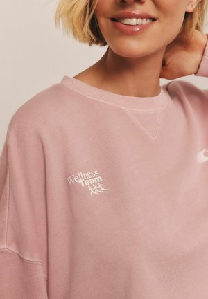 Helles pinkes Sweatshirt aus Baumwollmischung, mit rundem Ausschnitt und überschnittenen Schulternähten. "Wellness Team"-Logo in Weiß auf der linken Brust.