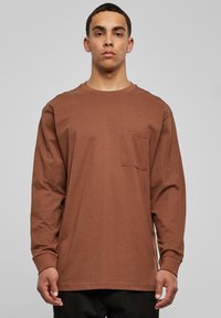 Camiseta de manga larga marrón hecha de algodón, con un cuello redondo y un bolsillo en el pecho, con un ajuste relajado y una textura suave.