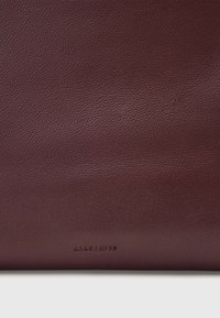 Viininpunainen nahkamateriaali, jossa on teksturoitu pinta; alareunassa on hillitty brändäys. Sileä viimeistely ja hillitty kiilto.