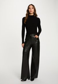Top a maniche lunghe a costine nera abbinato a pantaloni ampi in ecopelle nera a vita alta. I pantaloni presentano tasche e chiusura con bottone frontale.