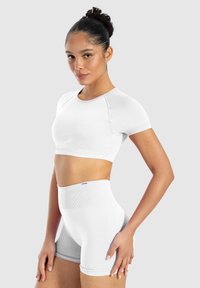 Weißes sportliches Crop-Top mit kurzen Ärmeln und passenden hochgeschnittenen Shorts. Glatte Textur mit gerippten Akzenten. Schlichtes, elegantes Design.