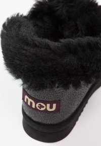 Zwarte laarzen met een gevoerde voering van vacht en een textuur van grijs aan de buitenkant. Beschikt over een paarse patch met het "mou" logo en een zwarte rubberen zool. Ronde bovenkant ontwerp.